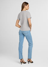 Woman wearing a gray t-shirt and light blue jeans on a white background. Back.