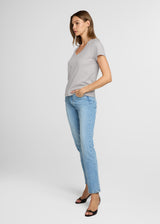 Woman wearing a gray t-shirt and light blue jeans on a white background. Side.