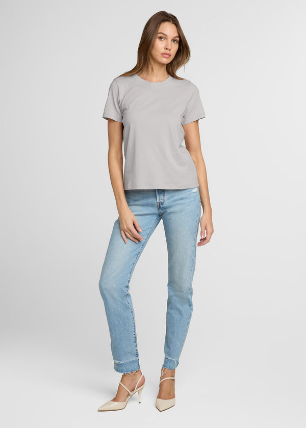 Woman wearing a gray t-shirt and light blue jeans on a white background. Front.