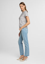 Woman wearing a gray t-shirt and light blue jeans on a white background. Side.
