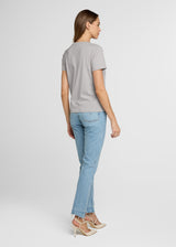 Woman wearing a gray t-shirt and light blue jeans on a white background. Back.