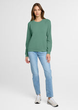 Woman wearing a green sweater and blue jeans on a white background. Front.