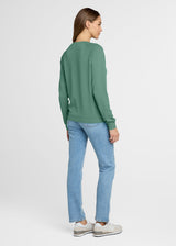 Woman wearing a green sweater and blue jeans on a white background. Back.