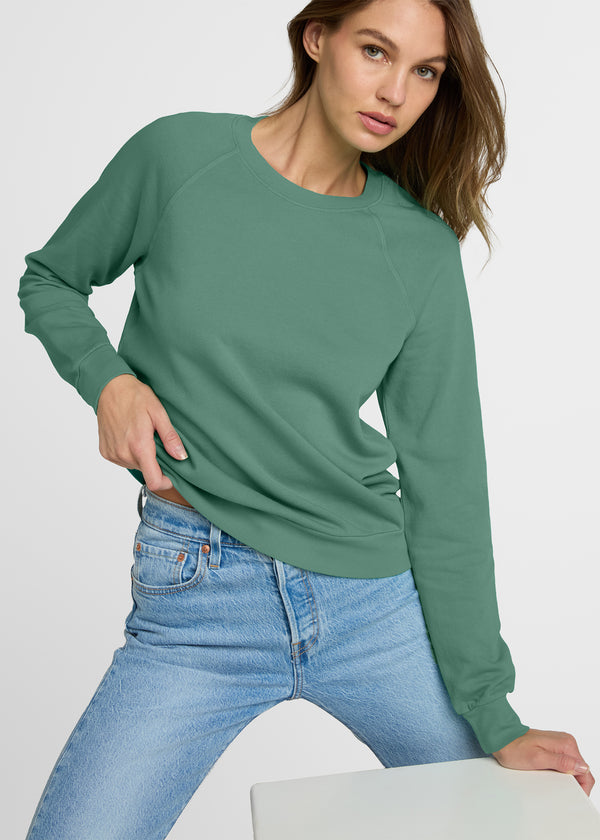 Woman wearing a green long-sleeve top and blue jeans on a white background. Detail.