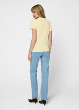 Woman wearing a yellow top and blue jeans on a white background. Back. 