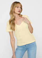 Woman wearing a yellow t-shirt and blue jeans against a plain background. Close up.