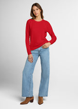 Woman wearing a red sweater and light blue jeans on a gray background