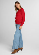 Woman wearing a red sweater and blue jeans on a white background. Side.