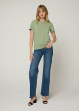 Woman in an untucked green t-shirt with dark denim and black wedge heels with her left hand in her pocket. 