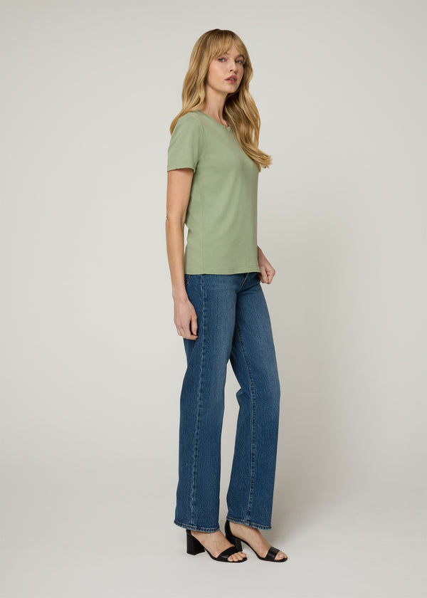 Side profile of woman in green t-shirt and dark denim jeans with her hands to her sides wearing black wedge heels. 