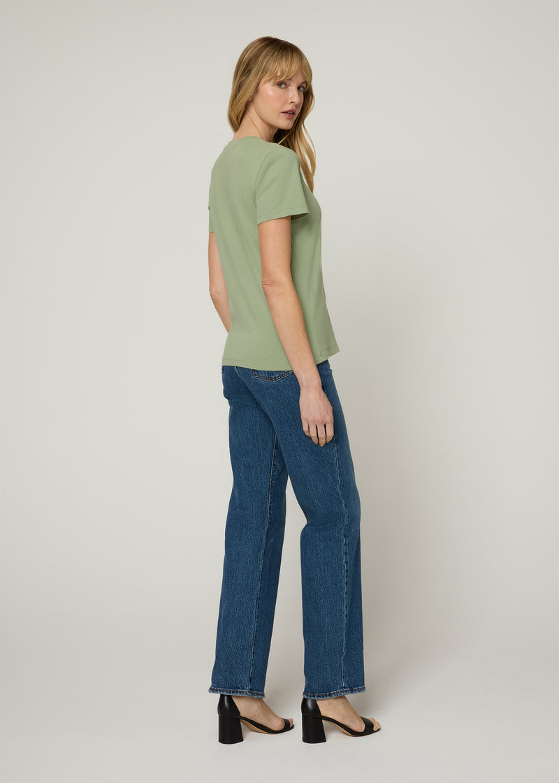 Back profile of a woman in a green t-shirt and dark denim wearing black wedge heels.