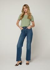 Woman in green t-shirt tucked into dark denim jeans, with her hands in her front pocket wearing black wedge heels. 