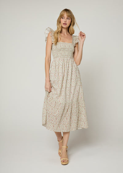 Woman in ivory floral print midi dress with smocked bodice and smocked flounce shoulders with a flowy tiered skirt wearing nude wedges. Front. 