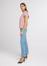 Woman wearing a pink top and blue jeans on a white background. Side.