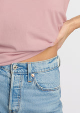 Person wearing a pink top and blue jeans on a plain background. Close up of modest midriff. 