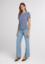 Woman wearing a blue top and light blue jeans on a white background. Side.