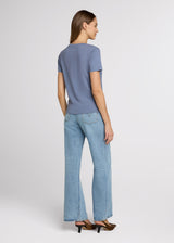 Woman wearing a blue top and light blue jeans on a white background. Back.