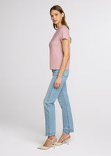 Woman wearing a pink top and light blue jeans on a white background. Side. 