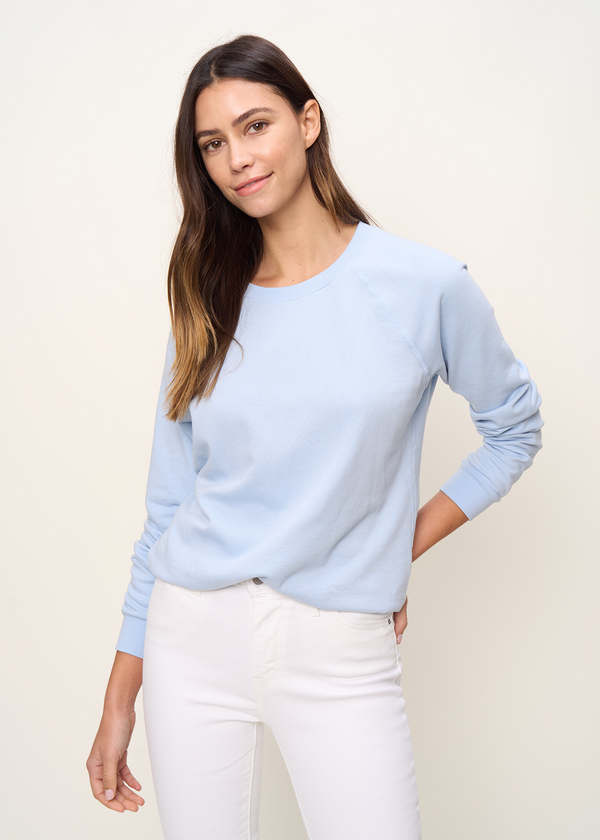 Woman in crewneck raglan sweatshirt made of organic and recycled cotton French Terry in color sky blue close up of raglan stitching detail paired in white denim