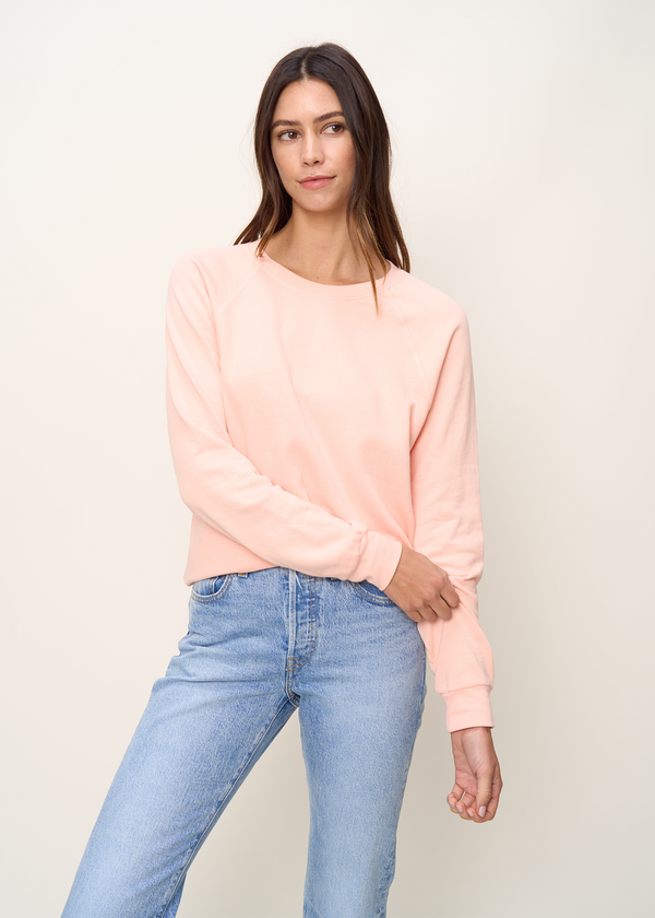 Woman in crewneck raglan sweatshirt made of organic and recycled cotton French Terry in color peach paired with blue denim