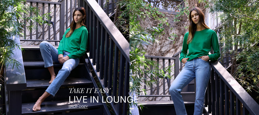 Woman in green sweatshirt and blue jeans sitting on an outdoor patio. 