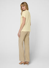 Woman wearing a light yellow top and beige pants on a white background. Back.
