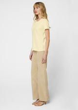 Woman wearing a light yellow top and beige pants on a white background. Side