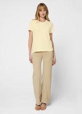 Woman wearing a light yellow top and beige pants on a white background