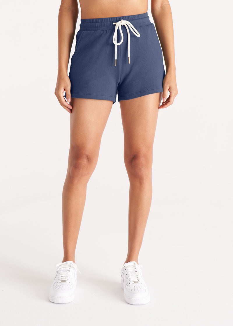 Woman in relaxed fit jogger shorts made of organic and recycled cotton French Terry with elastic waist, side pockets, and brass capped drawcords in color Midnight Navy, Front 