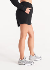 Woman in relaxed fit sweat shorts with elastic waist, side pockets, and interior drawcords made of organic and recycled cotton French Terry in color Onyx Black, Side
