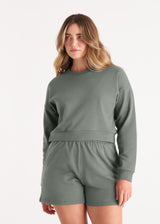 Woman in crewneck cropped sweatshirt with drop shoulders and length to midriff made of organic and recycled cotton French Terry in color Thyme Green, Front