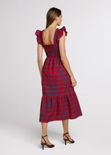 Woman in red plaid midi dress and black heels with her hands at her side. Back.
