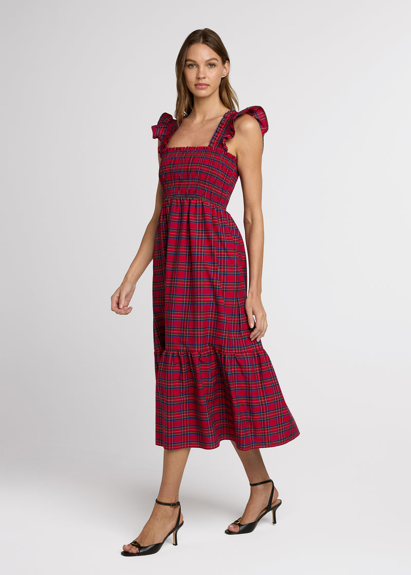 Woman in red plaid midi dress and black heals with her hands at her side. Side.