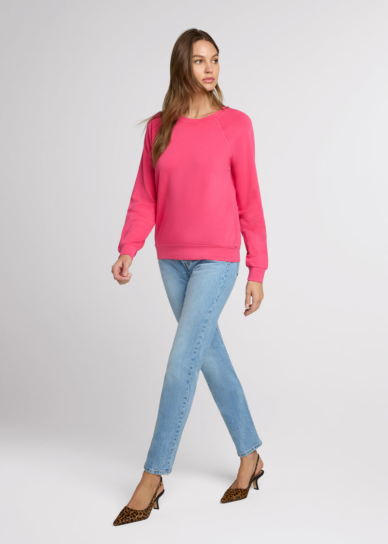 Woman in pink sweatshirt and blue denim and animal print heels. Side.