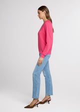 Woman in pink sweatshirt and light denim with her hands at her side. Side.