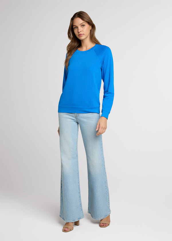 Woman in blue raglan sweatshirt and light blue denim standing with her hands at her side. Front. 