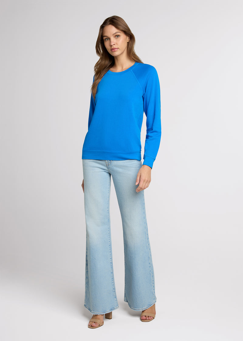Woman in blue raglan sweatshirt and light blue denim standing with her hands at her side. Front. 