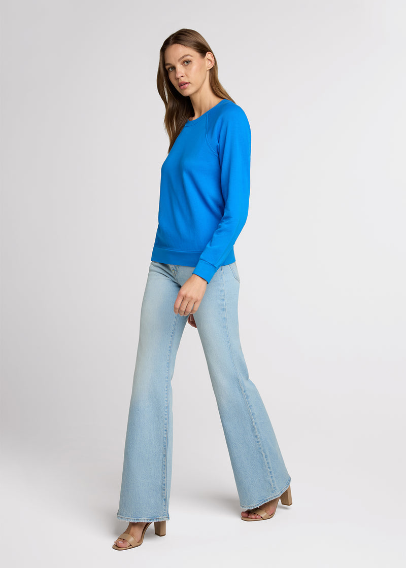 Woman in blue raglan sweatshirt and light denim with her hands at her side. Side. 