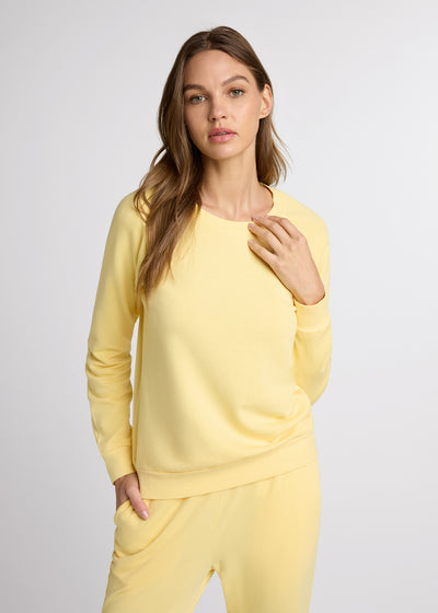 Woman in yellow sweatshirt and yellow sweatpant with one hand at the collar of her sweatshirt while the other hand is in her pant pocket.