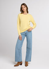 Woman in yellow sweatshirt and blue denim with one hand in her pant pocket and the other at her side. Front.