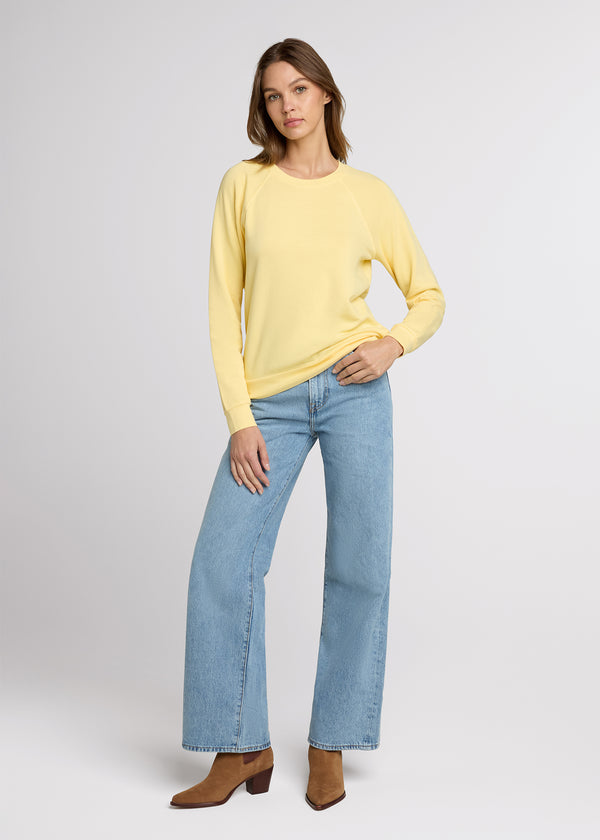 Woman in yellow sweatshirt and blue denim with one hand in her pant pocket and the other at her side. Front.