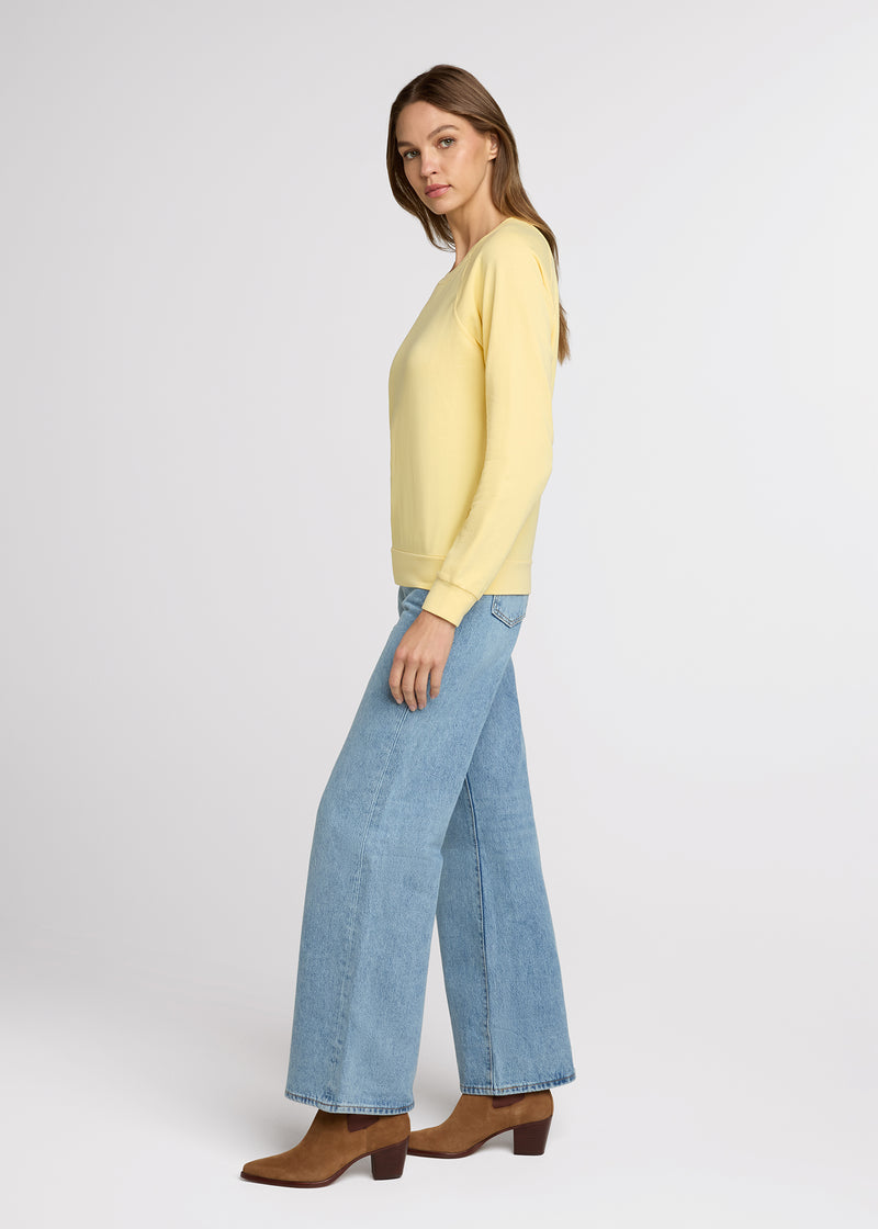 Woman in yellow sweatshirt and blue jeans standing with her hands at her side. Side. 