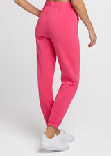 Woman in pink sweatpant standing with one hand at her hip and the other at her side. Back.