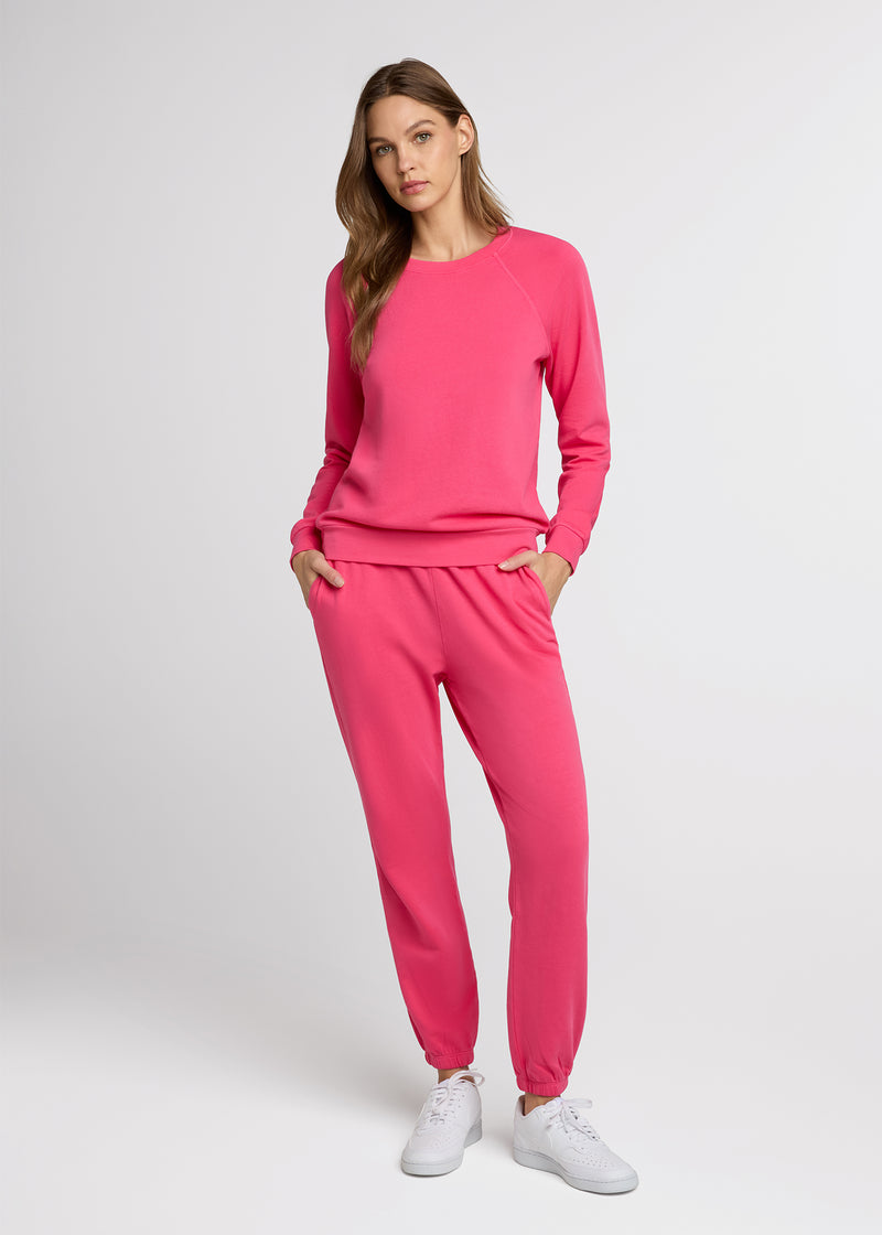 Woman in pink sweatpant and pink sweatpant standing with her hands in her pockets.