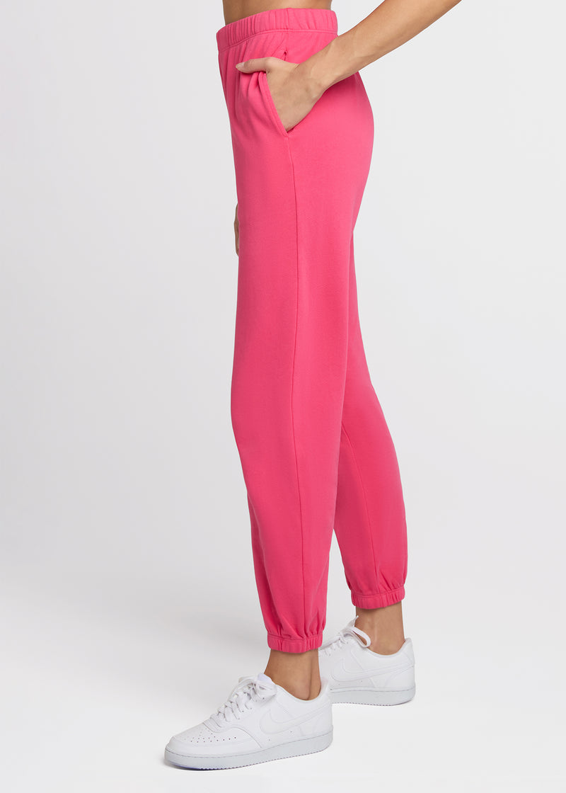 Woman in pink sweatpant standing with her hands in her pockets. side