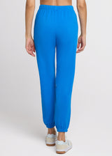 Woman in blue sweatpant standing with her hands at her side. Back.