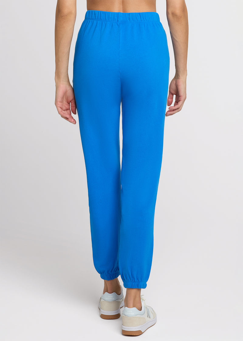 Woman in blue sweatpant standing with her hands at her side. Back.