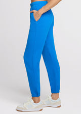 Woman in blue sweatpant with her hands in her pocket. Side.