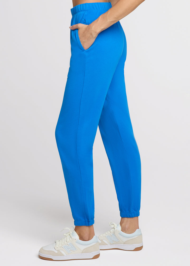 Woman in blue sweatpant with her hands in her pocket. Side.