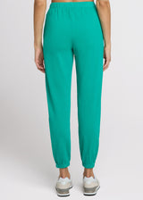 Woman in green sweatpant standing with her hands at her side. Back. 